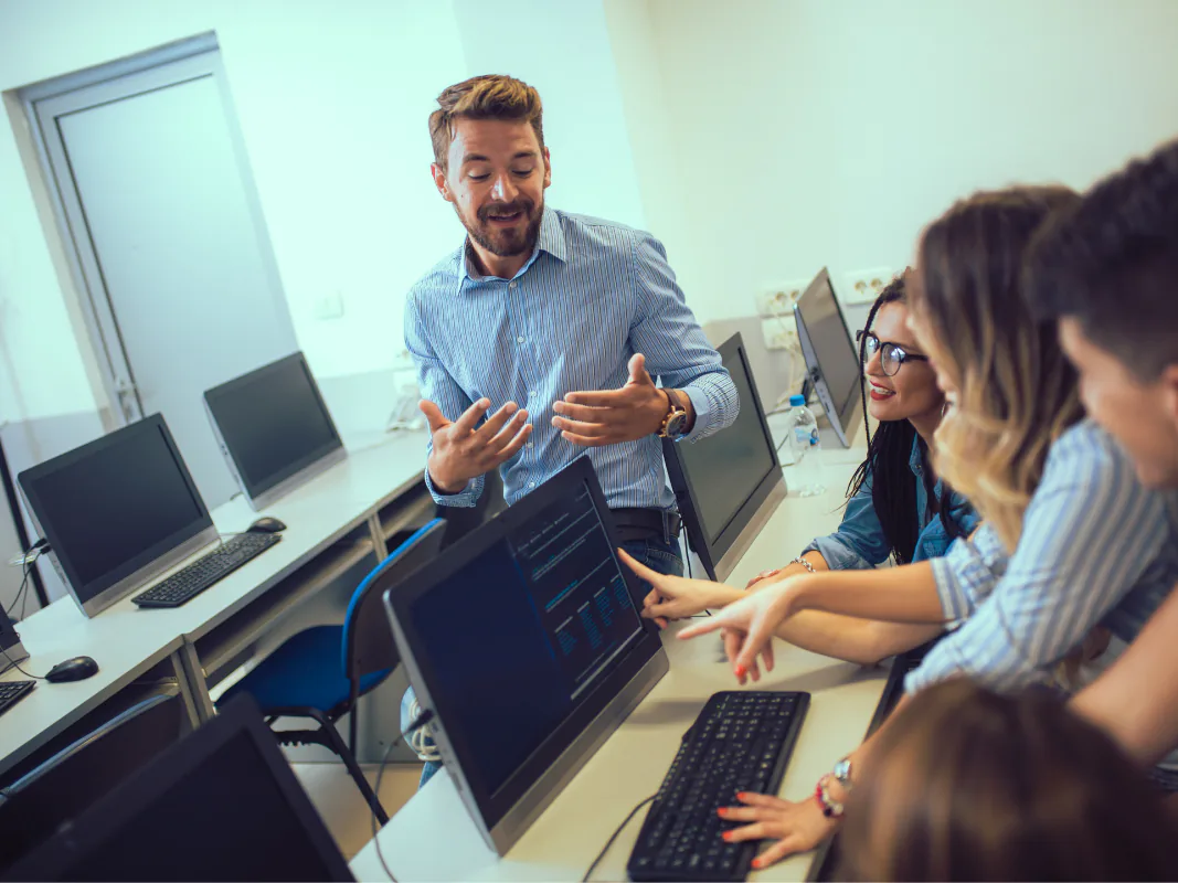Un docente e alcuni studenti davanti ai monitor di un laboratorio di informatica